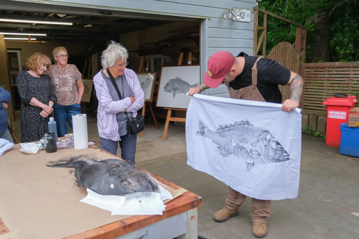 Artist Tim Li holding a gyotaku print he has just taken from an actual fish on the table in front of him.
